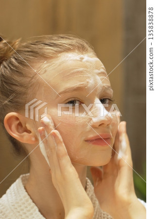 Closeup Smiling Teen Girl gently Applies Cleansing Foam, Facial Cleanser to face in modern bathroom. Beauty Routine, Skincare and Personal Hygiene. Close-up of Caucasian Gen Alpha Girl Washing Face Closeup Smiling Teen Girl gently Applies Cleansing Foam, Facial Cleanser to face in modern bathroom. Beauty Routine, Skincare and Personal Hygiene. Close-up of Caucasian Gen Alpha Girl Washing Face 135838878