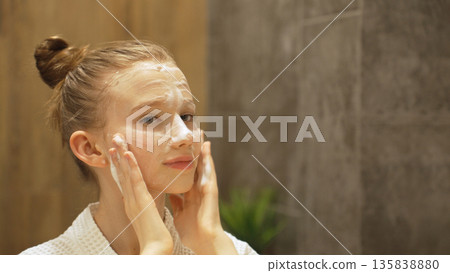 Smiling Teen Girl gently Applies Cleansing Foam, Facial Cleanser to face in modern bathroom. Beauty Routine, Skincare and Personal Hygiene. Close-up of Blonde Caucasian Gen Alpha Girl Washing Face Smiling Teen Girl gently Applies Cleansing Foam, Facial Cleanser to face in modern bathroom. Beauty Routine, Skincare and Personal Hygiene. Close-up of Blonde Caucasian Gen Alpha Girl Washing Face 135838880
