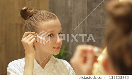 Cute Teen Girl Applying Facial Serum With Dropper in Modern Bathroom, Looking in Mirror. Blonde Caucasian Gen Alpha Girl and Beauty Routine. Daily Skincare Routine Cute Teen Girl Applying Facial Serum With Dropper in Modern Bathroom, Looking in Mirror. Blonde Caucasian Gen Alpha Girl and Beauty Routine. Daily Skincare Routine 135838883