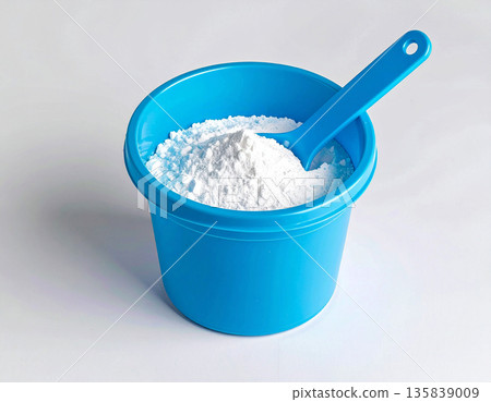 Home cleaning blogs. Pile of powdered detergent in blue plastic container with a measuring spoon on a white background. Home washing and cleaning. Home cleaning blogs. Pile of powdered detergent in blue plastic container with a measuring spoon on a white background. Home washing and cleaning. 135839009