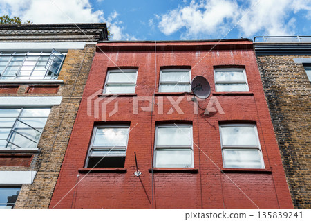 Red brick building facade with windows and a satellite dish in London. Red brick building facade with windows and a satellite dish in London. 135839241