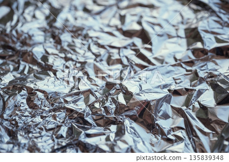 Crumpled aluminum foil surface reflecting light, creating abstract metallic textures 135839348