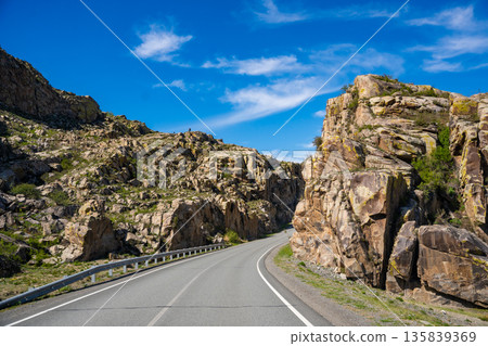 Asphalt road passing through stone cliffs at Stone Gates Chuysky Trakt Altai Russia. Iconic mountain pass framed by towering rocky formations. Asphalt road passing through stone cliffs at Stone Gates Chuysky Trakt Altai Russia. Iconic mountain pass framed by towering rocky formations. 135839369