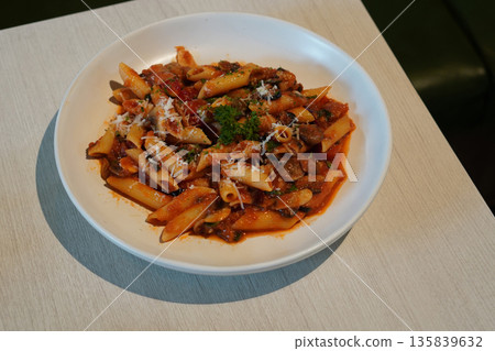 pasta spaghetti tossed in a rich, chunky tomato-based sauce, mushroom and Cheese and vegetables on white ceramic plate, on wooden table, green leather chair background, food, health, copy space 135839632