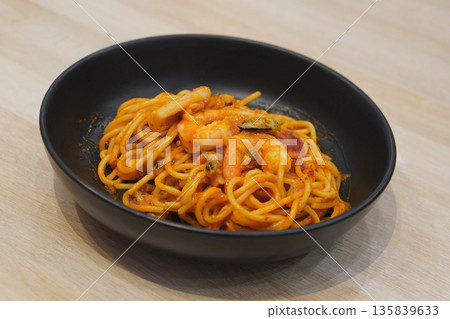 spaghetti with seafood, shrimp, tomato ketchup, cockles in a black ceramic bowl, on wooden floor background, food, object, copy space 135839633