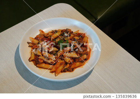 top view hot pasta spaghetti tossed in a rich, chunky tomato-based sauce, mushroom and Cheese and vegetables on white ceramic plate, on wooden table, green leather chair background, food, health, copy 135839636