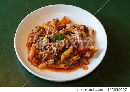 top view hot penne pasta spaghetti tossed in a rich, chunky tomato-based sauce, mushroom and Cheese and vegetables on white ceramic plate, leather green background, food, health, copy space top view hot penne pasta spaghetti tossed in a rich, chunky tomato-based sauce, mushroom and Cheese and vegetables on white ceramic plate, leather green background, food, health, copy space 135839637