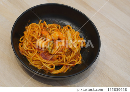 top view hot spaghetti with seafood, shrimp, tomato ketchup, cockles in a black ceramic bowl, on wooden floor background, food, object, copy space 135839638