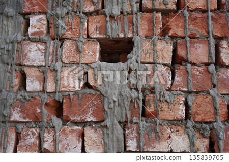Untidy brickwork with gaps between uneven chopped bricks unfilled with cement mortar. Gray cement stains as melted candle wax on a hand-molded red brick. Abstract background in the style of punk rock. Untidy brickwork with gaps between uneven chopped bricks unfilled with cement mortar. Gray cement stains as melted candle wax on a hand-molded red brick. Abstract background in the style of punk rock. 135839705