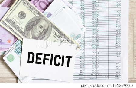 The inscription "DEFICIT" on a notebook with banknotes from different countries.  135839739