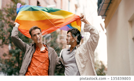 Gay male couple holding rainbow flag celebrating pride 135839803