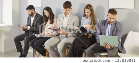 Group of business people preparing for job interview or meeting while checking documents or gadgets. 135839811