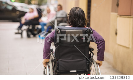 Person with disability pushing wheelchair on city street 135839813