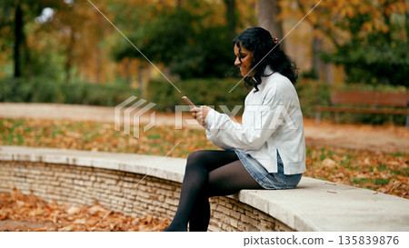 Indian woman using smartphone in autumn park Indian woman using smartphone in autumn park 135839876