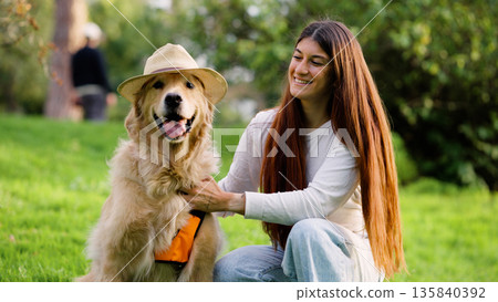 Golden retriever dog wearing hat with woman in park 135840392