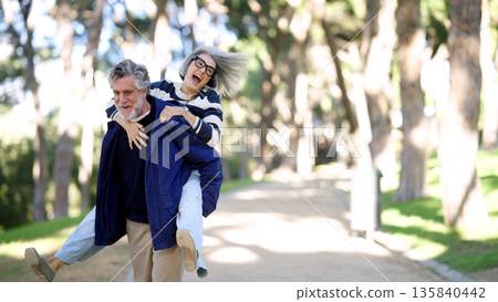 Senior couple enjoying piggyback ride in park 135840442
