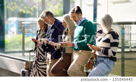 Diverse mature people waiting while using smartphones Diverse mature people waiting while using smartphones 135840445