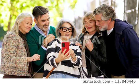 Diverse senior friends using smartphone outdoors enjoying technology Diverse senior friends using smartphone outdoors enjoying technology 135840446