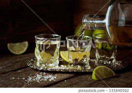 Tequila with salt and lime slices on a silver tray. Tequila with salt and lime slices on a silver tray. 135840502