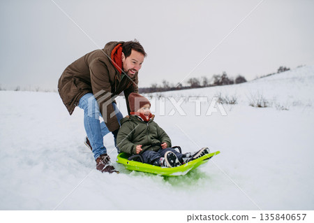 Dad and child bobbing downhill on snow slider. 135840657