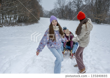 Daughters pulling parents on sled through winter landscape. Daughters pulling parents on sled through winter landscape. 135840693