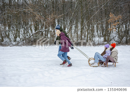 Parents pulling daughters on sled through winter landscape. 135840696