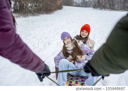 Parents pulling daughters on sled through winter landscape. 135840697