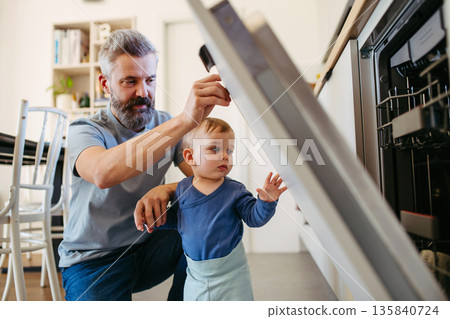 Father caring for toddler son while doing household chores. 135840724