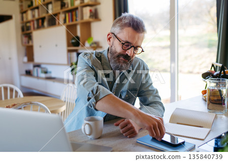 Man working from homeoffice, scrolling on phone. Man working from homeoffice, scrolling on phone. 135840739