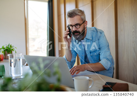 Man working from home while on phone call. Man working from home while on phone call. 135840740