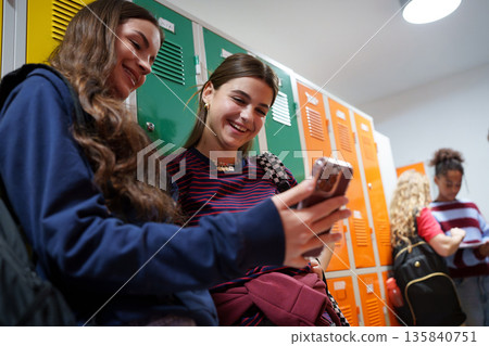 Teen students looing at phone in school hallway by lockers. Teen students looing at phone in school hallway by lockers. 135840751