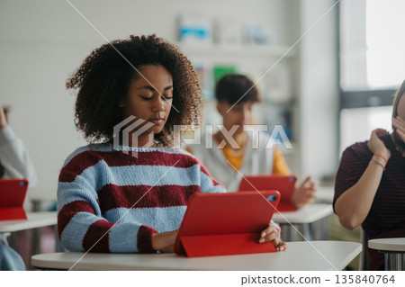 Teen student listening attentively during class while using digital tablet. Teen student listening attentively during class while using digital tablet. 135840764
