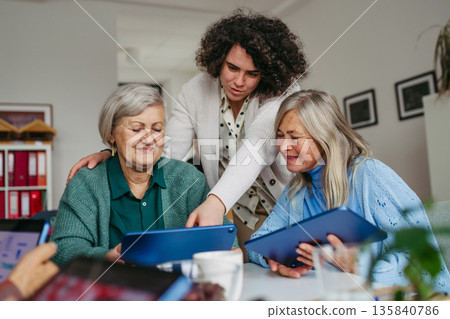 Volunteer teaching seniors how to work with digital tablet. 135840786
