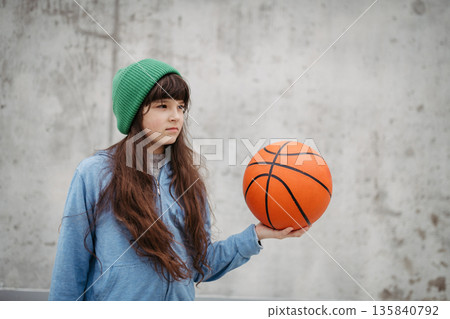 Sad girl alone in the city, want to play basketball. Young girl spending free time alone in the city, no friends, holding basketball. Sad girl alone in the city, want to play basketball. Young girl spending free time alone in the city, no friends, holding basketball. 135840792