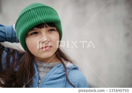 Outdoor portrait of cute young girl with beanie hat. Girl with long hair standing on playground in the city. Outdoor portrait of cute young girl with beanie hat. Girl with long hair standing on playground in the city. 135840793