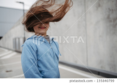 Outdoor portrait of young girl with long hair standing on playground in the city. 135840799