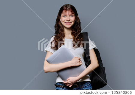 Portrait of beautiful girl teenage student holding laptop on gray background 135840806