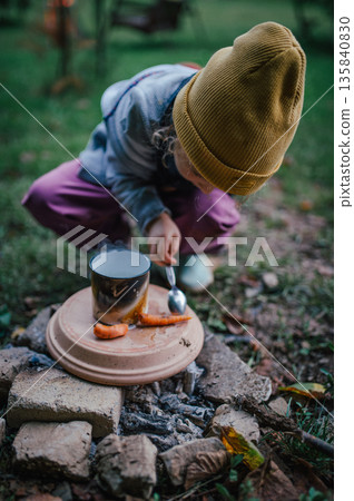 Little girl roasting vegetables on homemade campfire grill. Little girl roasting vegetables on homemade campfire grill. 135840830