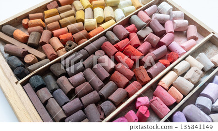 Different soft pastels sticks set in wooden case. Pink, red, yellow, brown colored sticks. Art multicolor background. 135841149