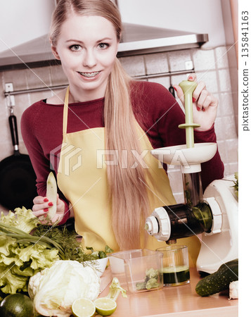 Woman in kitchen making vegetable smoothie juice 135841163