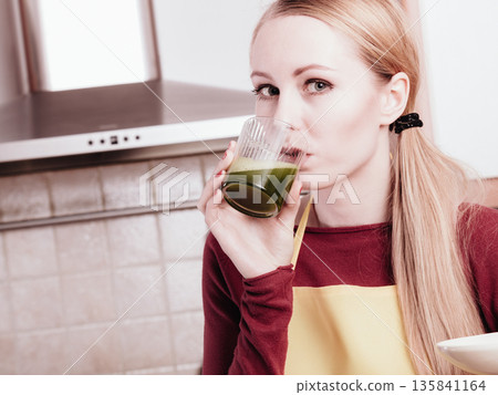 Woman in kitchen holding vegetable smoothie juice 135841164
