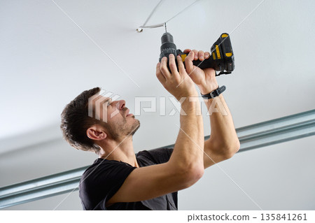 Man drilling ceiling with cordless power drill indoors 135841261