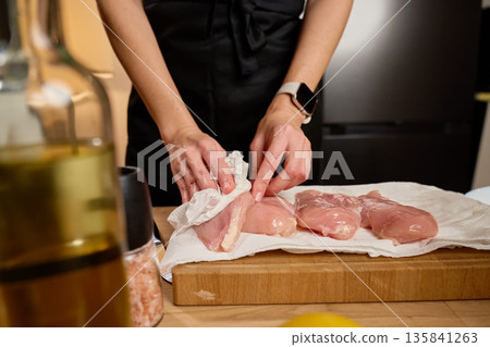 Woman drying raw chicken fillets with paper towels in home kitchen 135841263