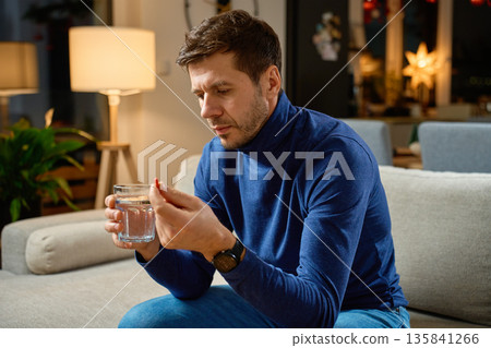 Man holding pill and glass of water at home 135841266