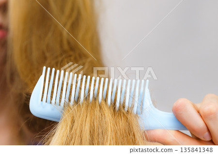 Blonde girl combing her long messy hair Blonde girl combing her long messy hair 135841348