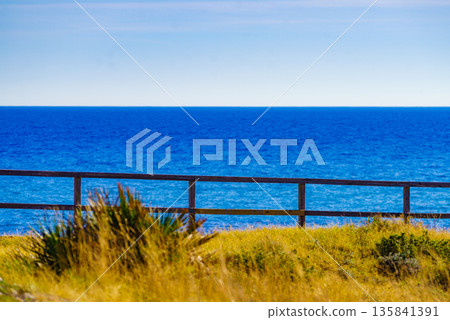 Seashore with fence and calm blue water 135841391
