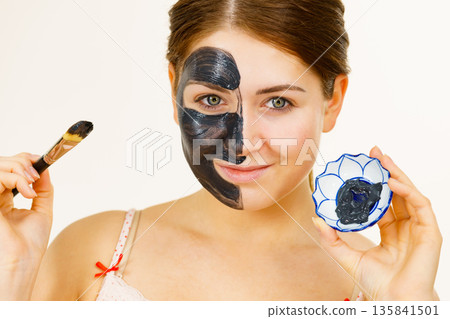 Female applying black mud mask to face 135841501