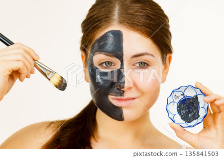 Female applying black mud mask to face Female applying black mud mask to face 135841503