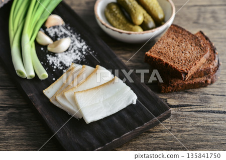 Pork fatback on a wooden cutting board with slices of rye bread, garlic, Pork fatback on a wooden cutting board with slices of rye bread, garlic, 135841750