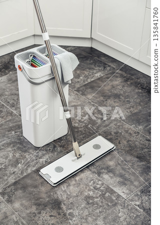 Cleaning supplies: mop, bucket with wringer sitting on tile floor in modern kitchen Cleaning supplies: mop, bucket with wringer sitting on tile floor in modern kitchen 135841760